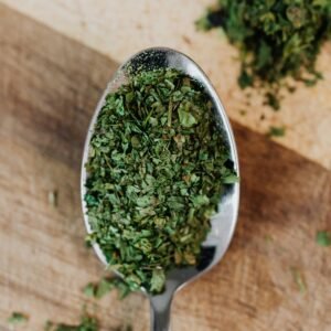 A detailed view of dried oregano herbs on a spoon over a wooden surface, showcasing freshness and texture.